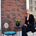 Fashionable woman in a black suit and sunglasses poses against a brick wall in Tallinn's urban setting.