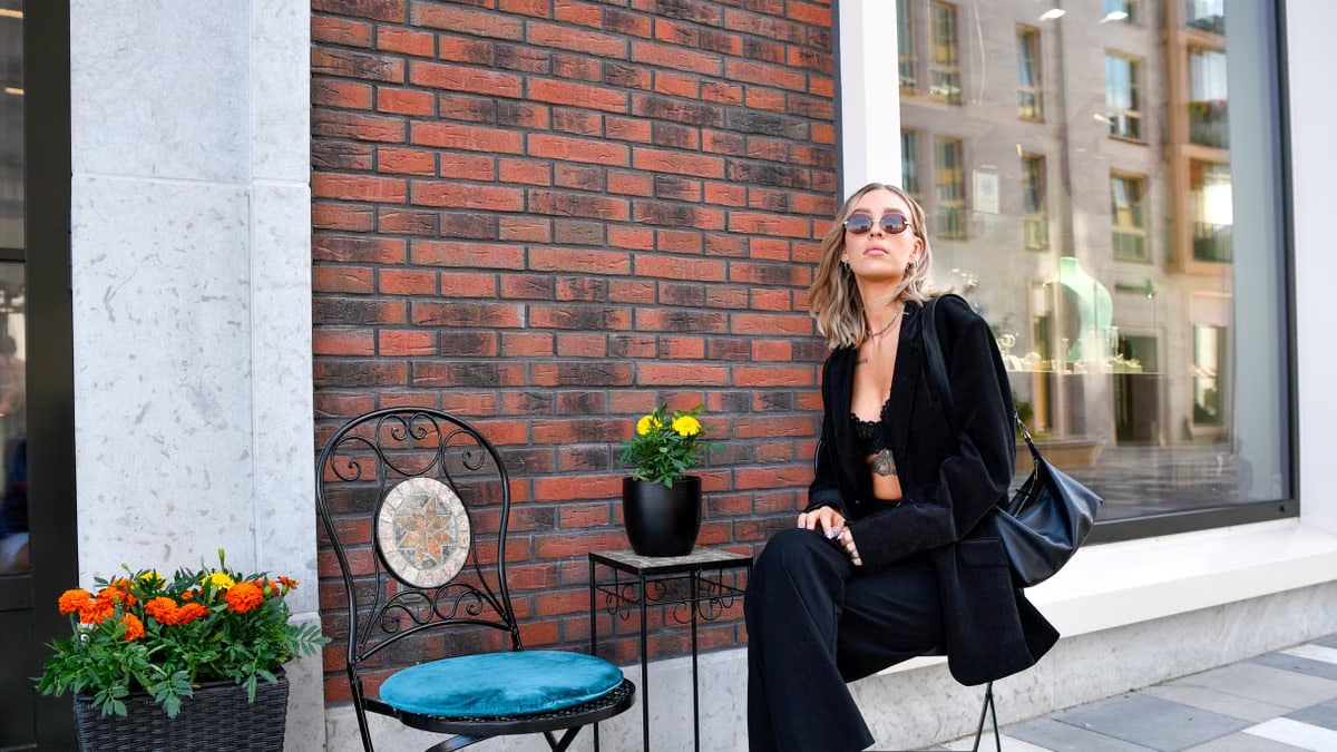 Fashionable woman in a black suit and sunglasses poses against a brick wall in Tallinn's urban setting.