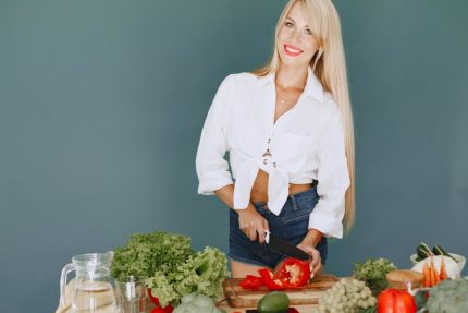 A smiling blonde woman chops vegetables, promoting healthy eating and lifestyle.